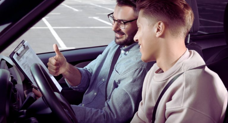 Jeune conducteur et examinateur souriants dans une voiture avec pouce leve