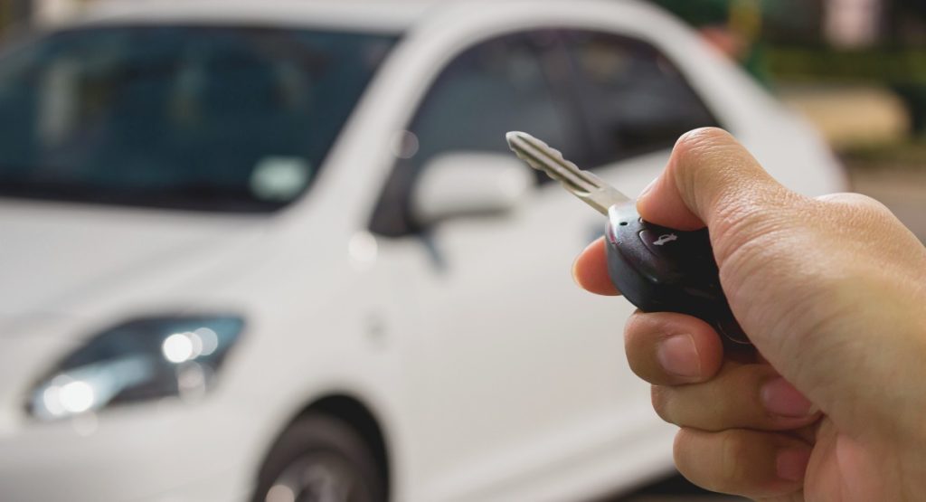 Main tenant une cle de voiture devant un vehicule blanc