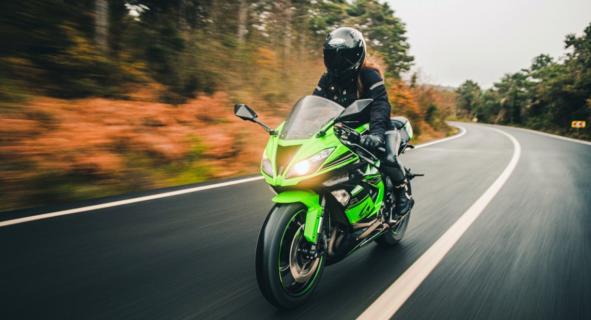 Motard casque integral sur moto sportive verte prenant un virage en automne